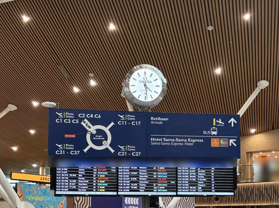クアラルンプール国際空港の到着ロビー。木の天井の下に丸い時計と案内板、発着の表示板が並ぶ