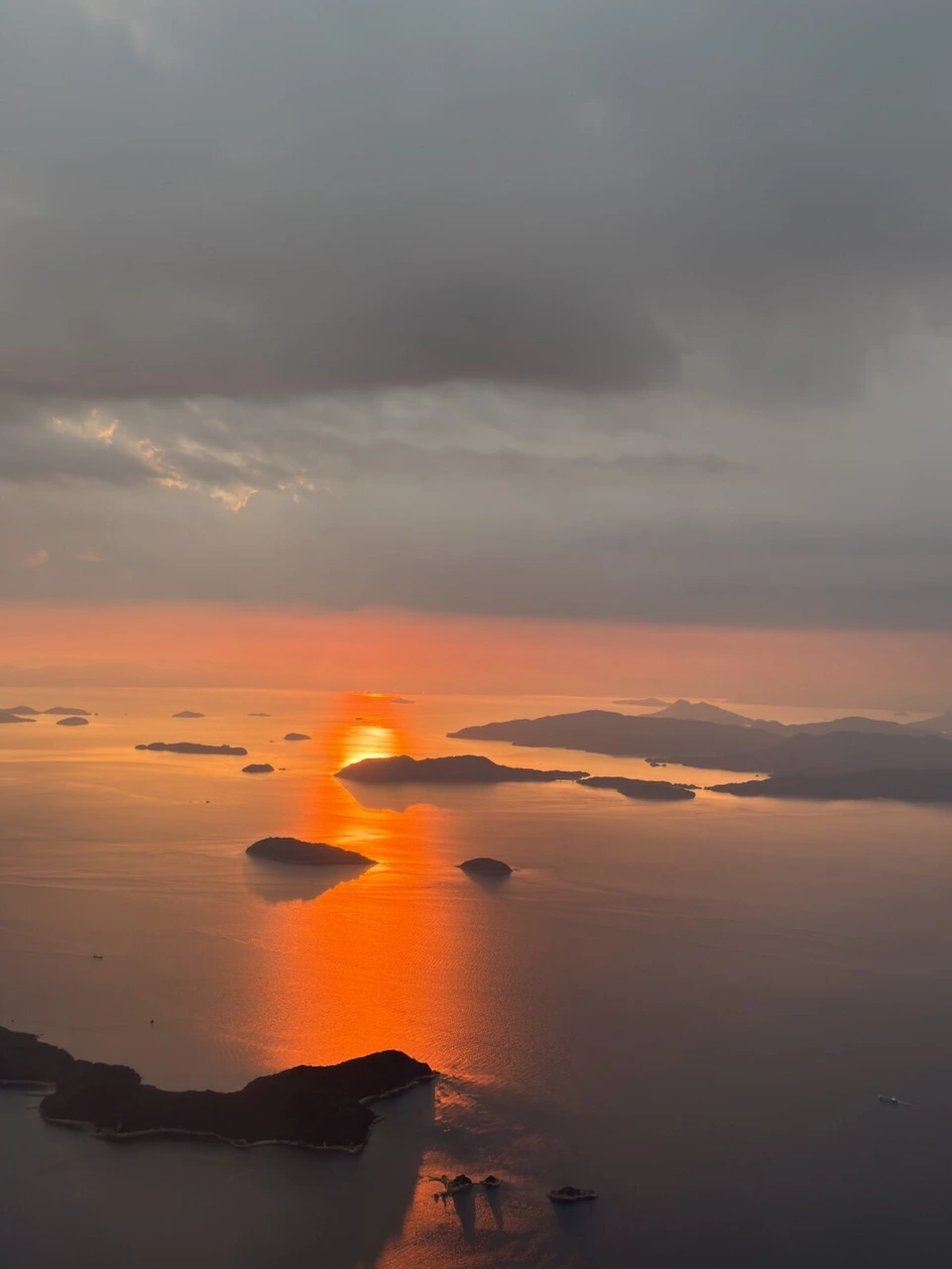 雲の下の瀬戸内海に沈む夕日と、オレンジ色に光る海面、島のシルエット