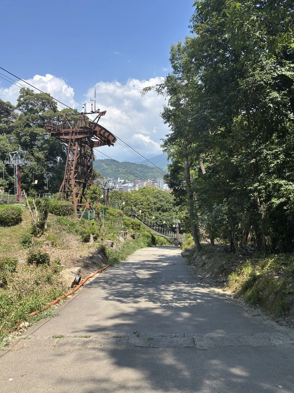 松山城のリフトの支柱と座席の横を通る坂道。奥に松山の街と山