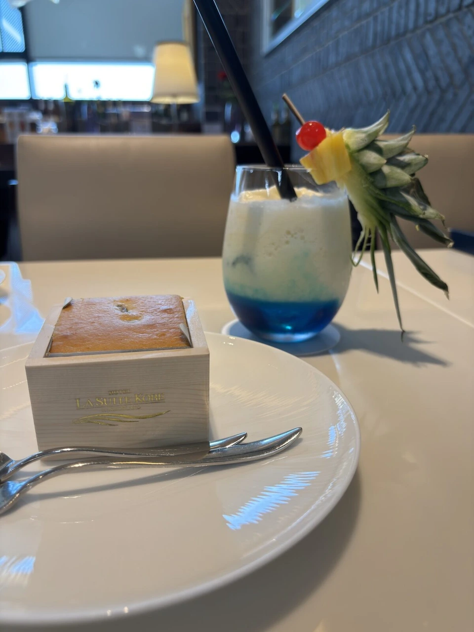 伊丹空港のカフェ。木の升に入ったケーキと、パイナップルを飾った青いグラデーションのドリンク
