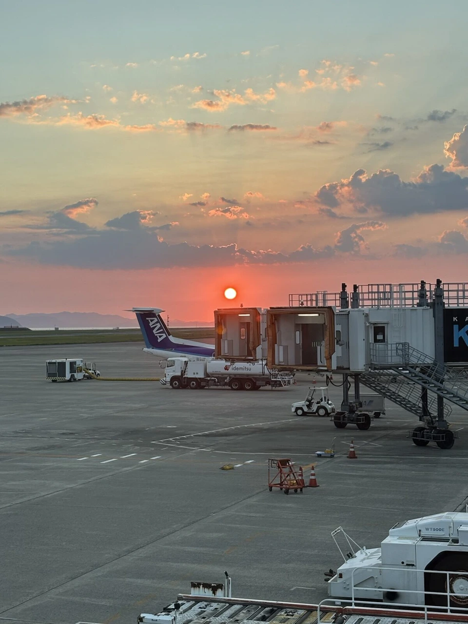 松山空港のエプロンに沈む夕日。ANAのプロペラ機の尾翼と搭乗橋、給油車
