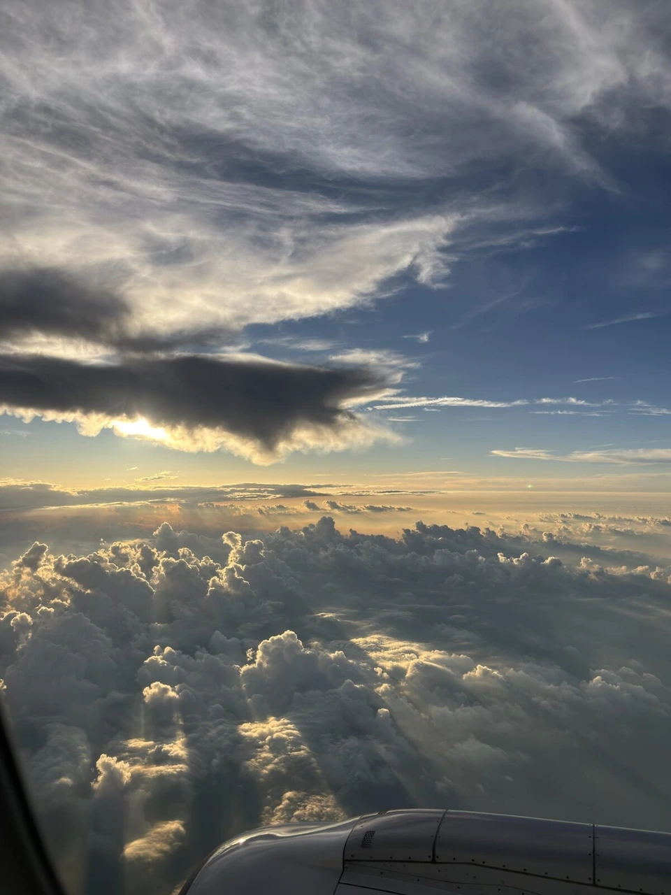 機窓から見た雲海と、雲の間から差す夕日の光。手前にエンジン