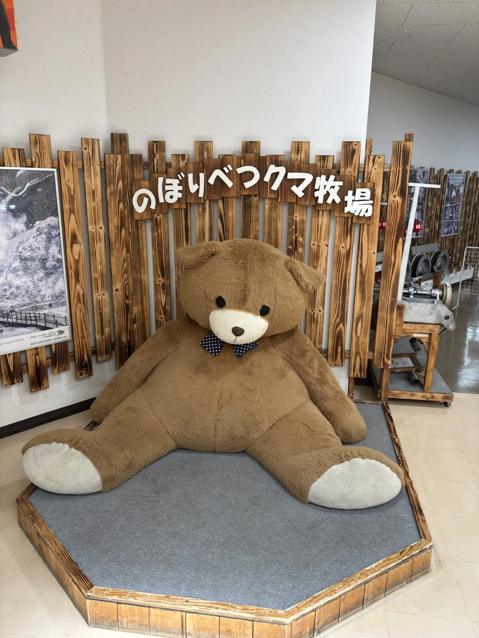 のぼりべつクマ牧場の文字の前に座る大きな茶色いクマのぬいぐるみ