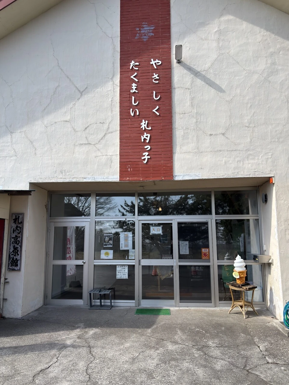 白い壁に「やさしく たくましい 札内っ子」と書かれた建物の入口と、ソフトクリームの置物