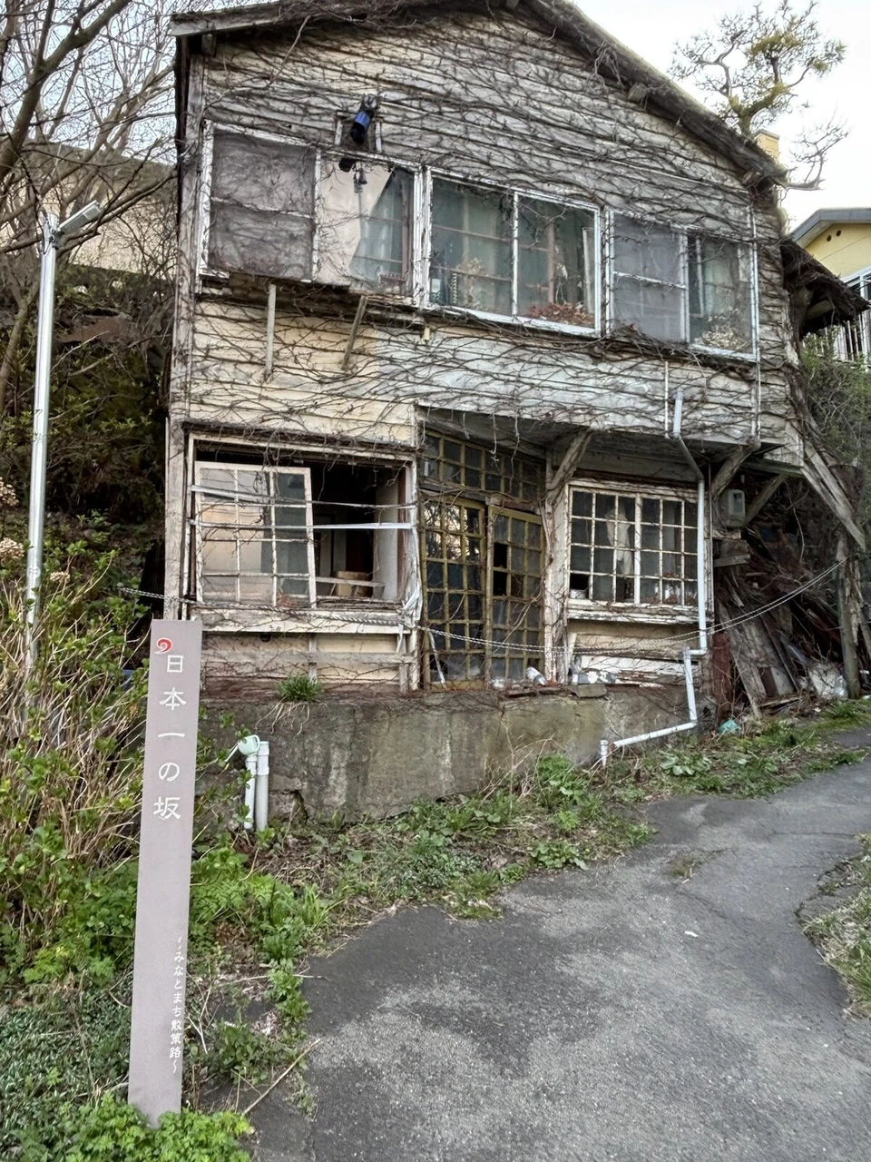 坂道の脇に建つ古い木造の家と「日本一の坂」の標柱