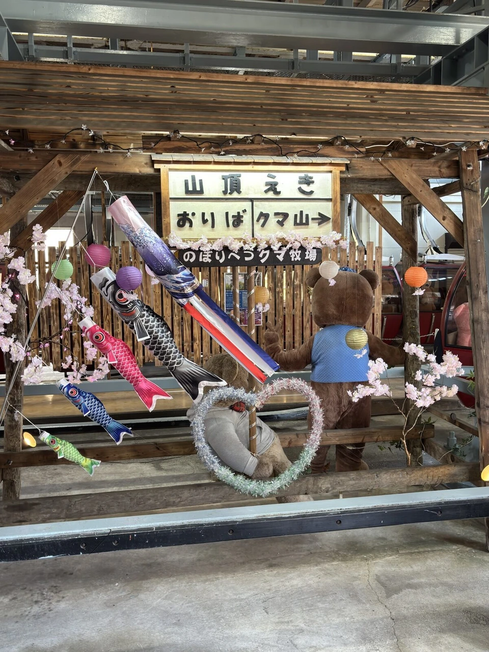山頂駅の「山頂えき おりば クマ山」の看板と、こいのぼりや桜の飾り、クマのぬいぐるみ