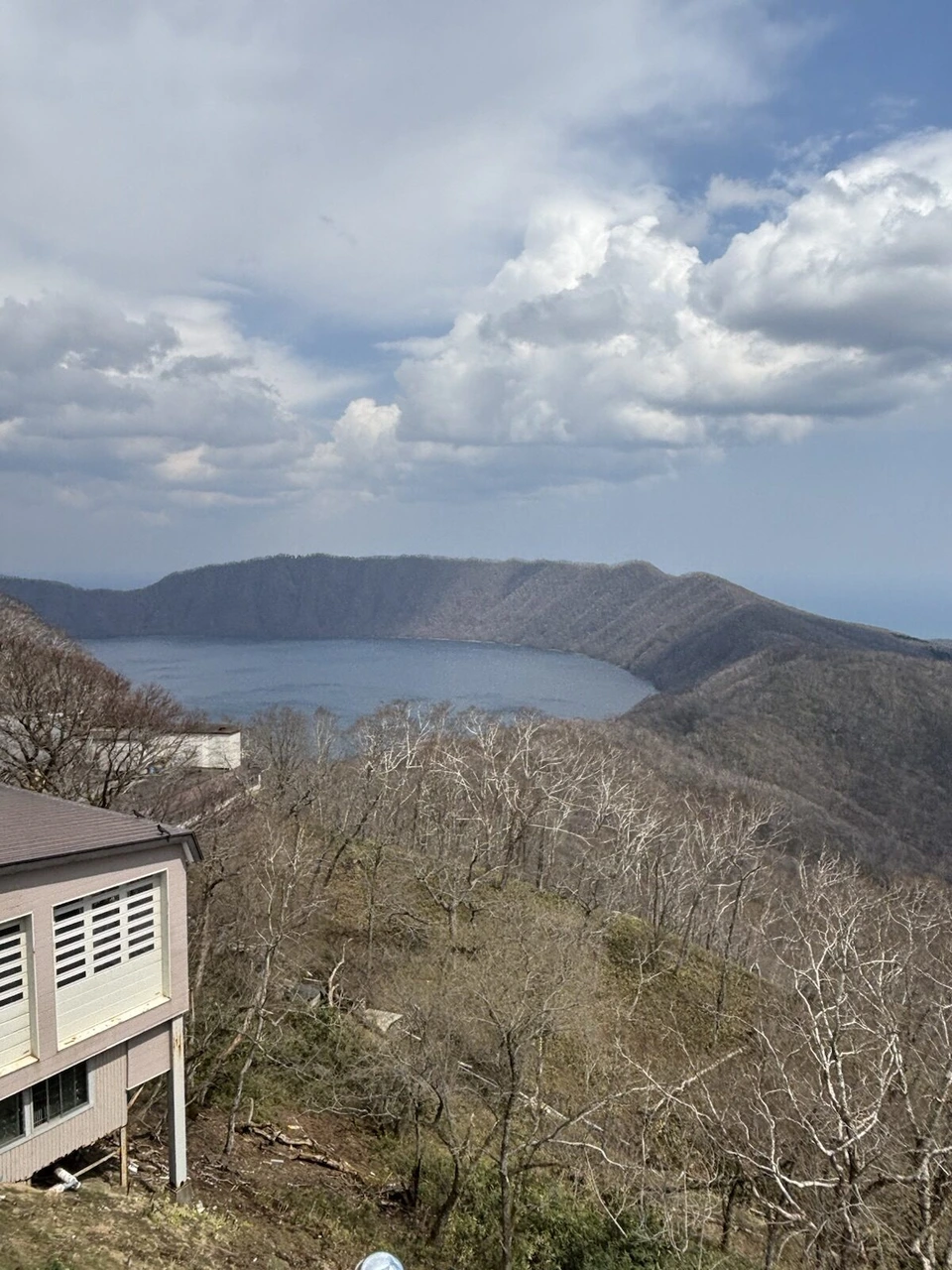 山頂から見たクッタラ湖。丸いカルデラ湖と周りの山、手前に建物の屋根