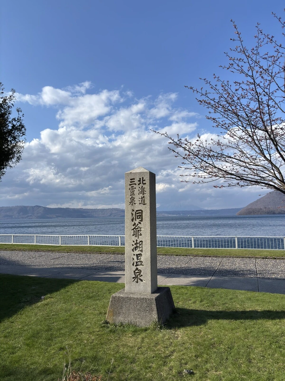 湖畔に立つ「北海道三霊泉 洞爺湖温泉」の石碑と桜の木、奥に洞爺湖