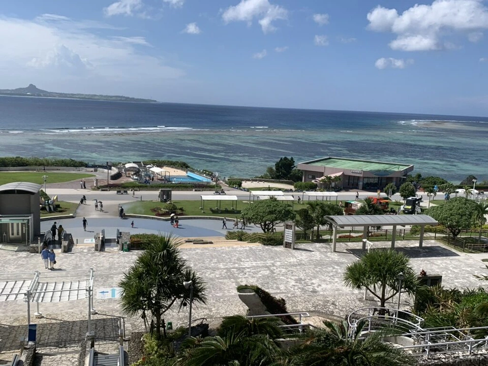 沖縄美ら海水族館の上から見た海洋博公園の広場とエメラルドグリーンの海、奥に伊江島