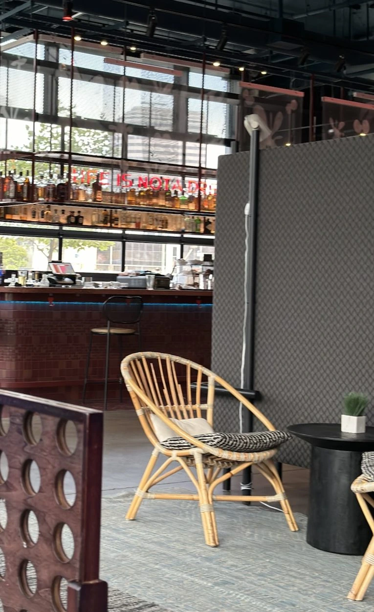 Moxy Oakland Downtownのロビーのバー。酒瓶が並ぶ棚と赤いネオンの文字、手前に籐の椅子と黒い丸テーブル