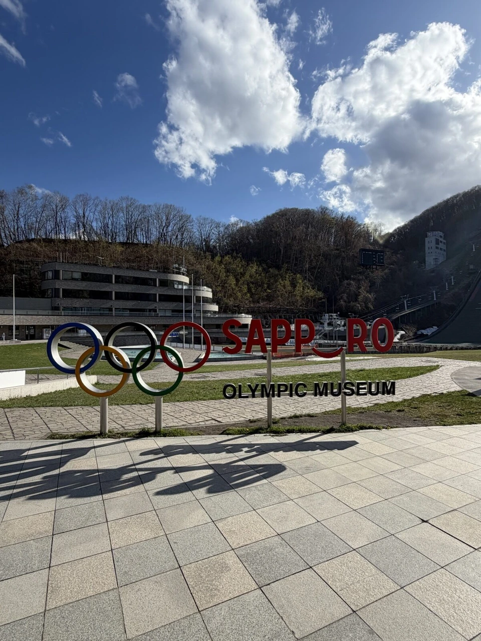 大倉山ジャンプ競技場の五輪マークとSAPPOROの文字のモニュメント、奥にジャンプ台