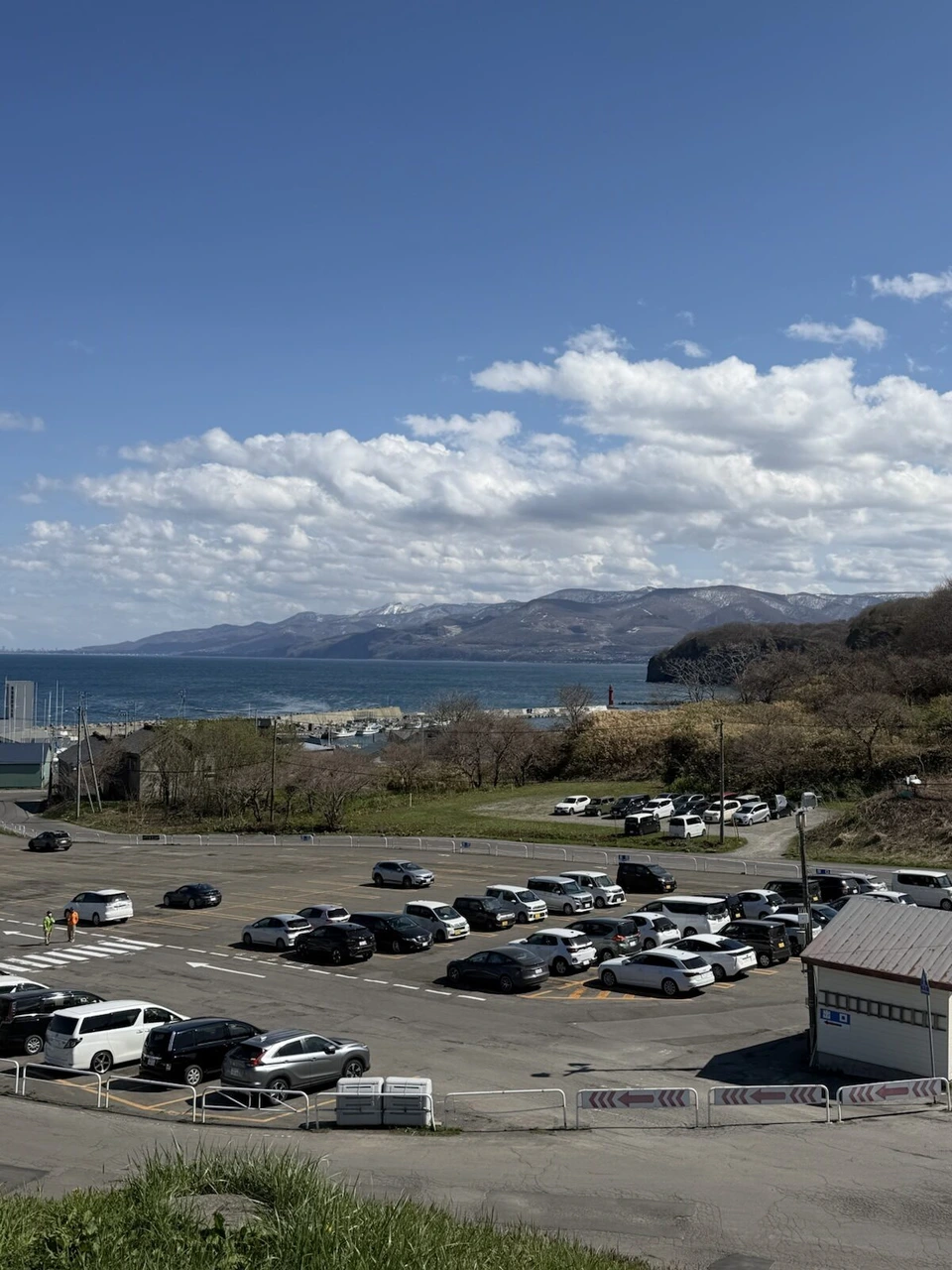 小樽・祝津の高台から見たおたる水族館の駐車場と、奥に広がる青い海と山