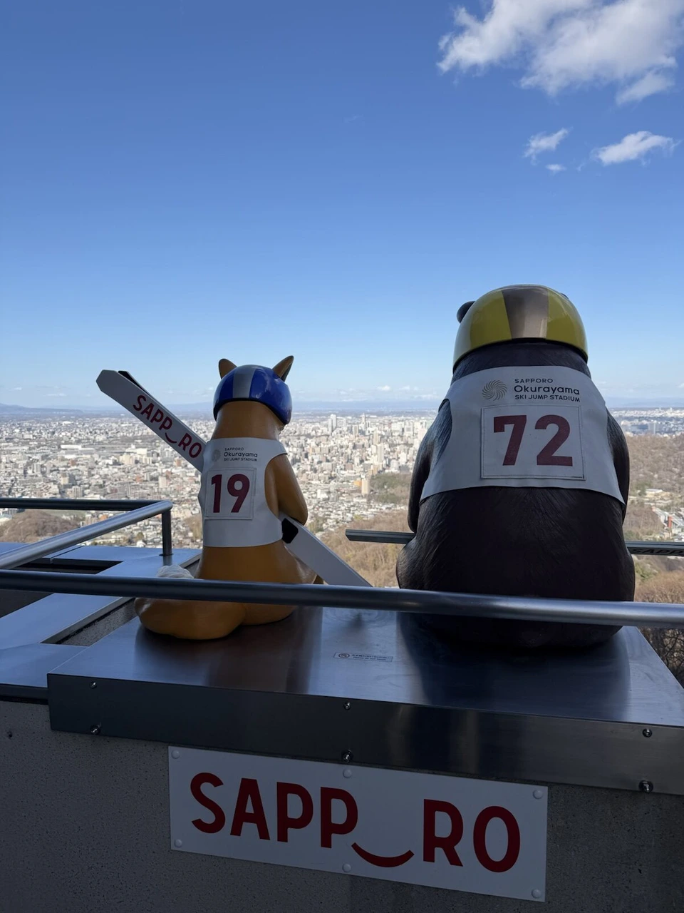 大倉山展望台の手すりの上に並ぶ、ゼッケンを付けたキツネとクマのキャラクターの像
