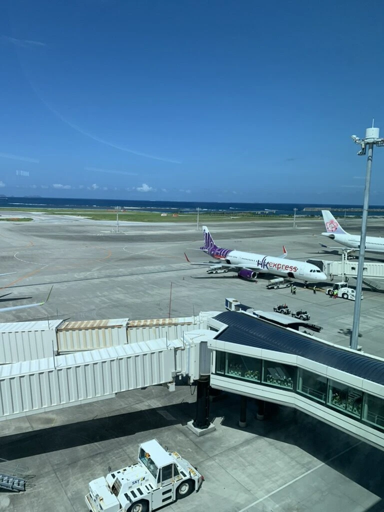 那覇空港の搭乗橋と駐機場、奥に海。紫色のHK Express機